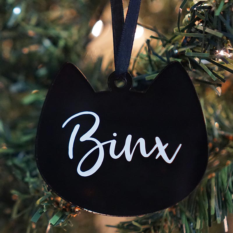 Image of cat-shaped ornament hanging by a ribbon on a tree